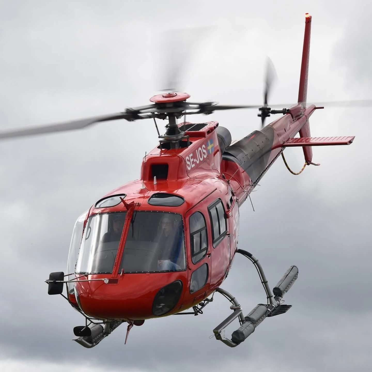 Red Airbus AS350 helicopter in the air with the Swedish flag on the side