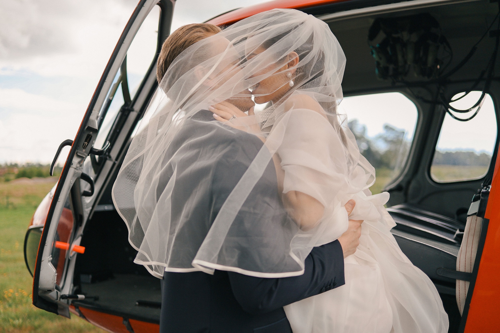Newlyweds embracing under the veil by the helicopter